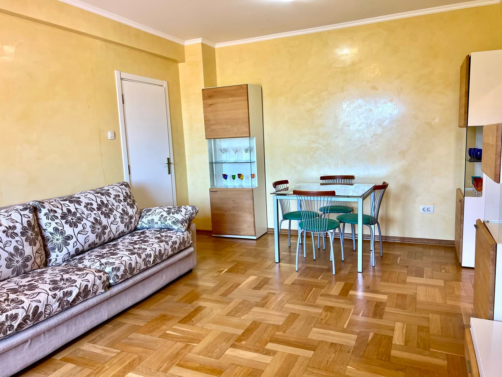 Living room in an apartment in Petrovac, Montenegro: floral-print sofa, dining area, and parquet flooring.