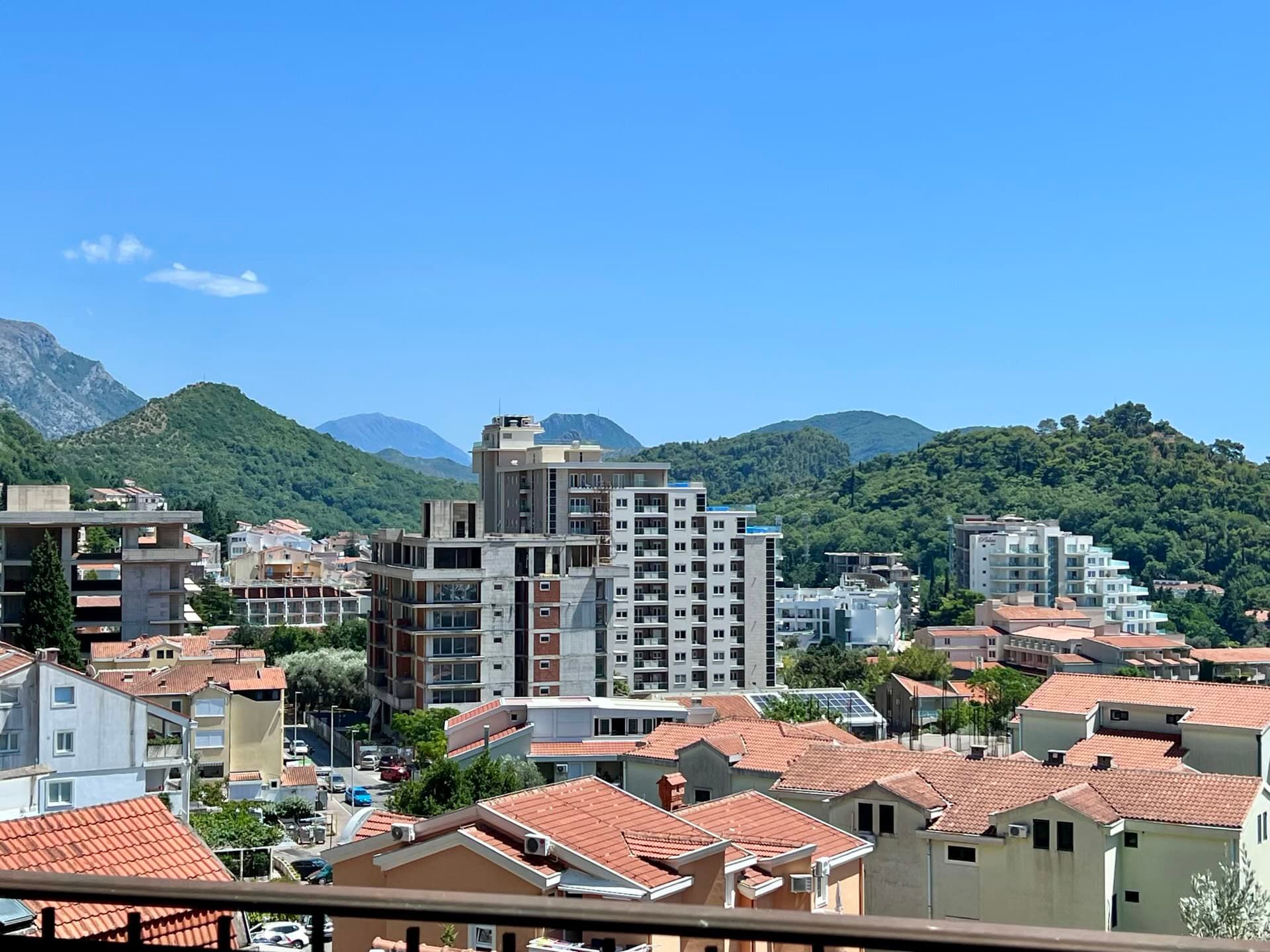 Panoramic view of the city of Petrovac in Montenegro with residential buildings, tiled roofs, and green mountains in the background.