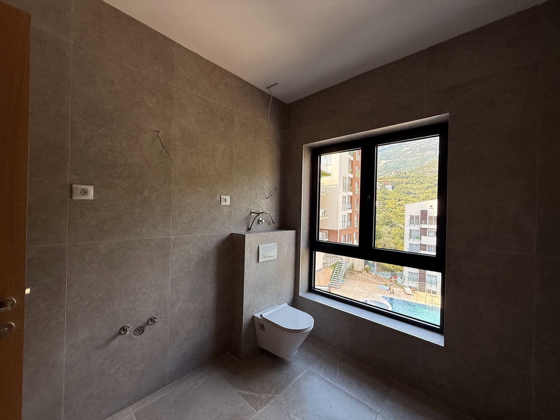 Modern bathroom in an apartment in Bečići, Montenegro: tiled finish, wall-hung toilet, and a view of the pool.