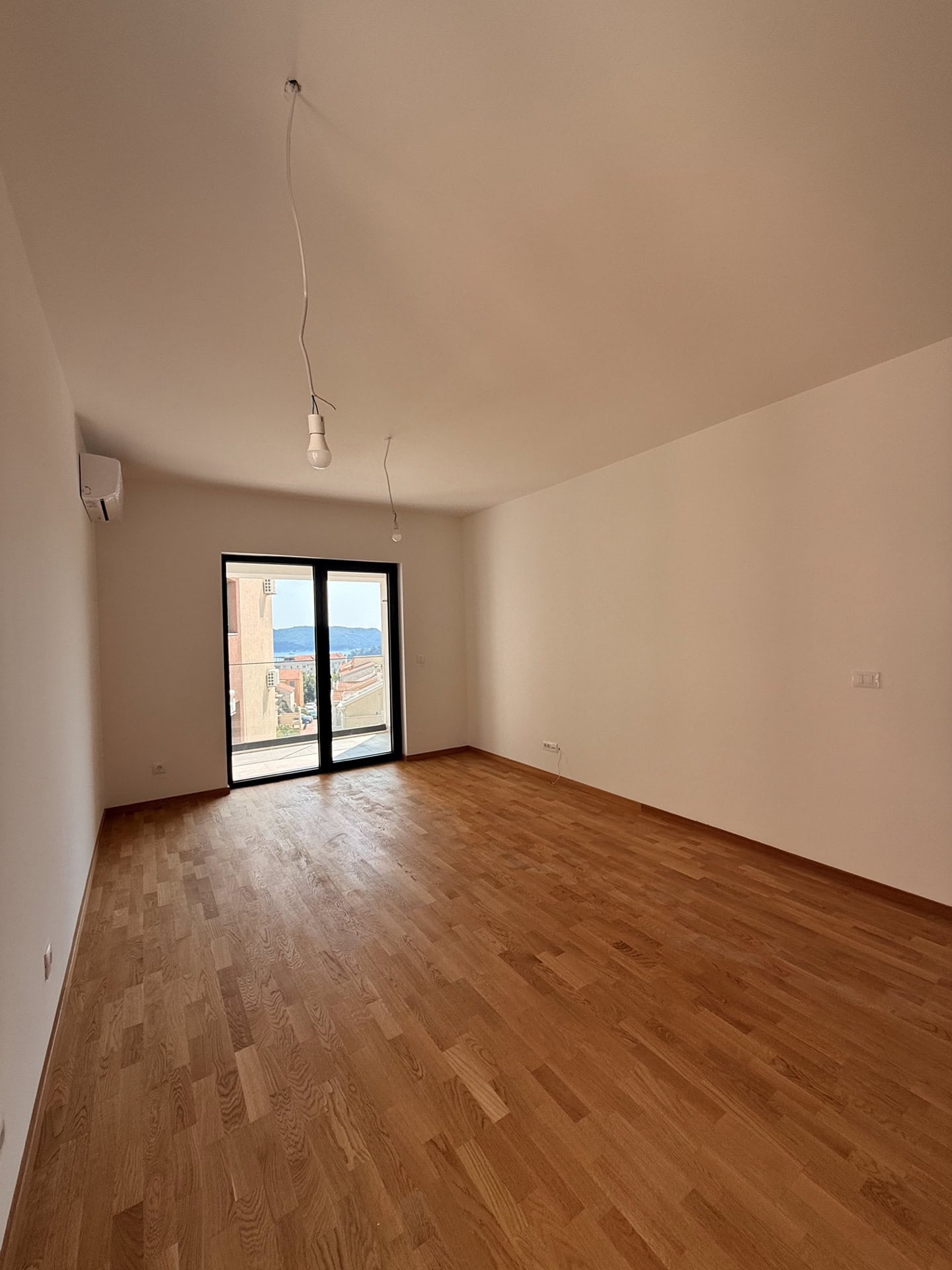 Bright living room with parquet flooring and access to the balcony in a new apartment in Bečići, Montenegro, with sea and mountain views.