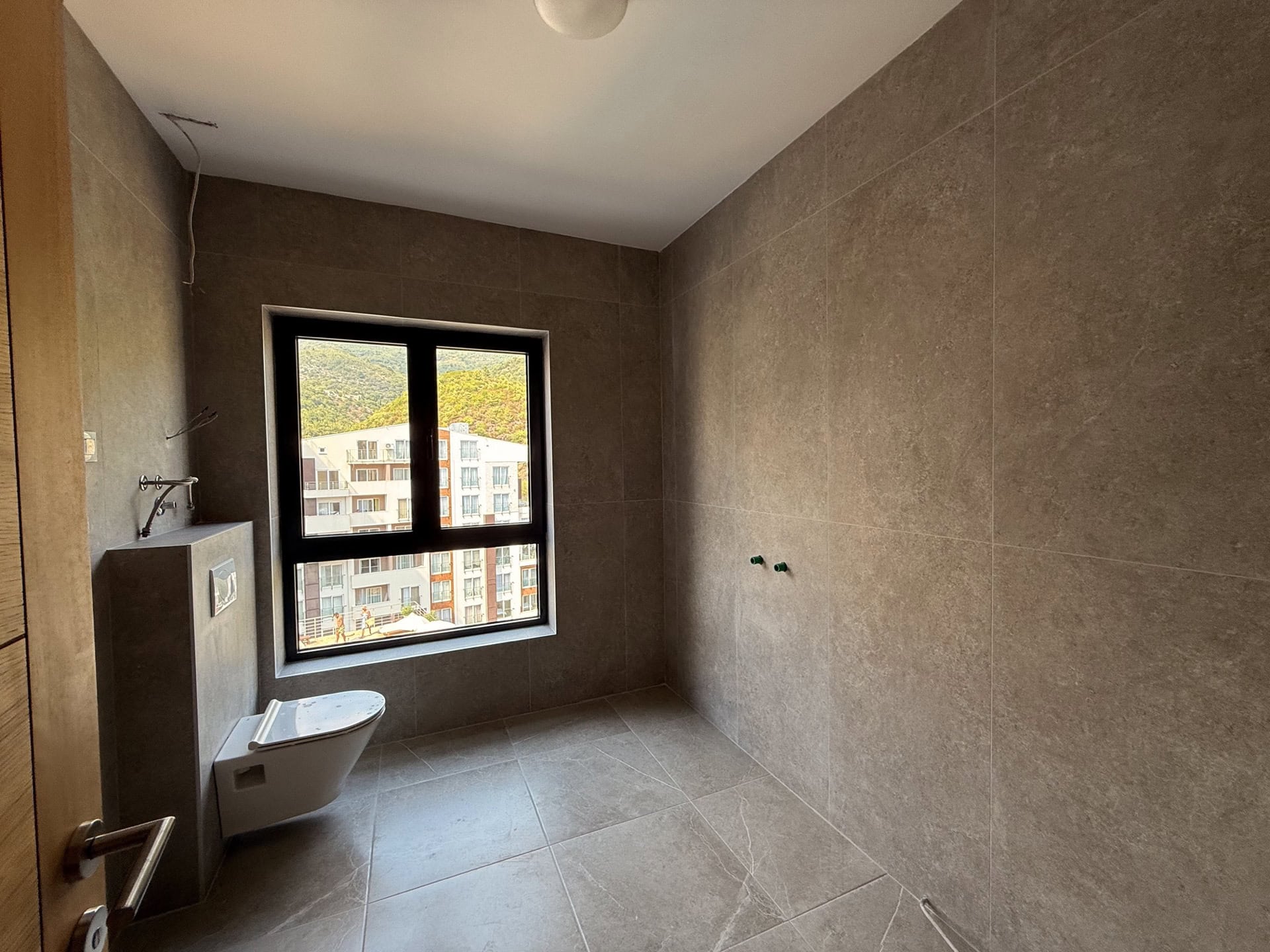 Modern bathroom in an apartment in Bečići, Montenegro: tiled finish, wall-hung toilet, and mountain view.