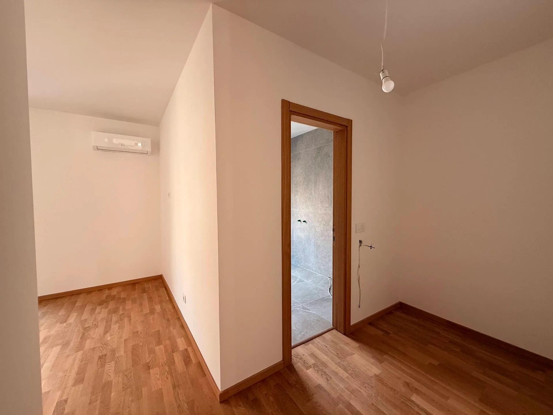 Empty room with wood flooring, AC unit, and open door leading to a tiled area.