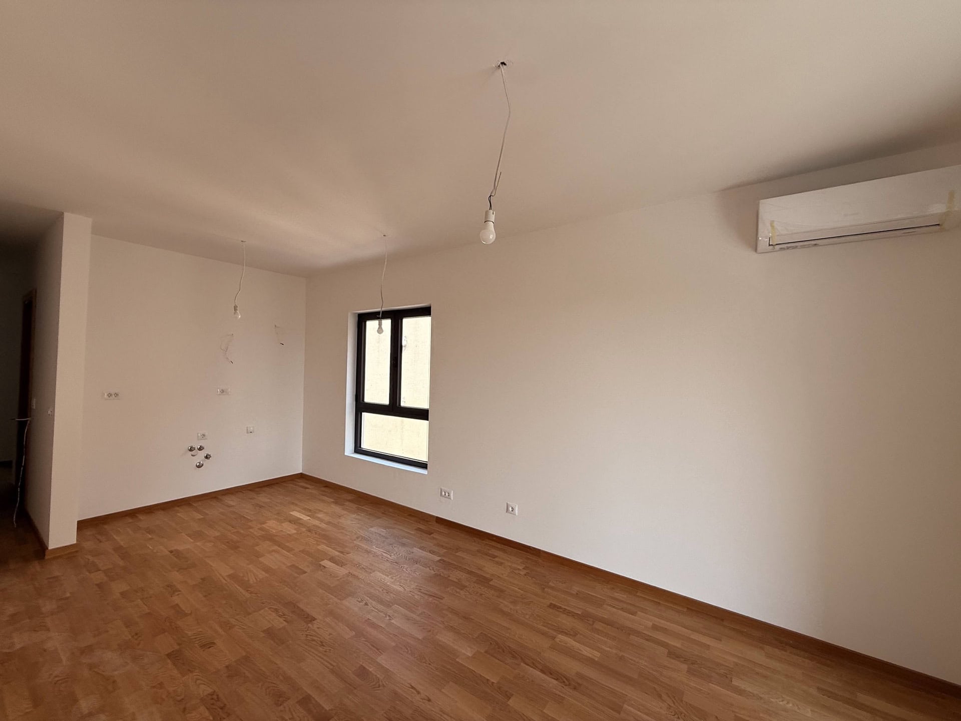 Bright living room in a new building in Bečići, Montenegro: parquet floor, white walls, air conditioner, and a panoramic window.