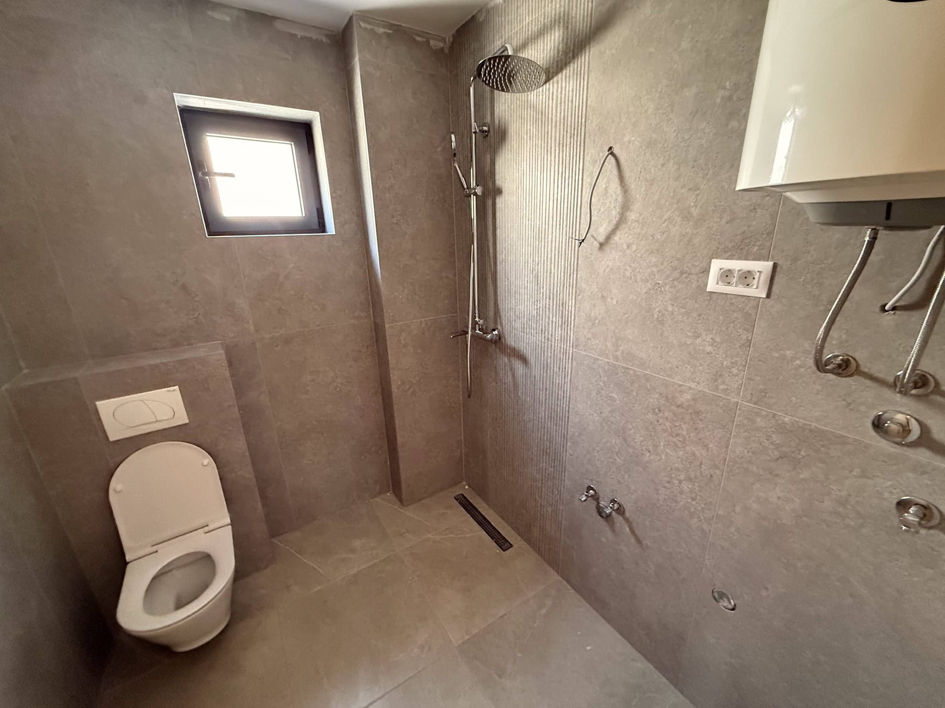 Modern bathroom in an apartment in Bečići, Montenegro: shower cabin, wall-hung toilet, and gray tiles.