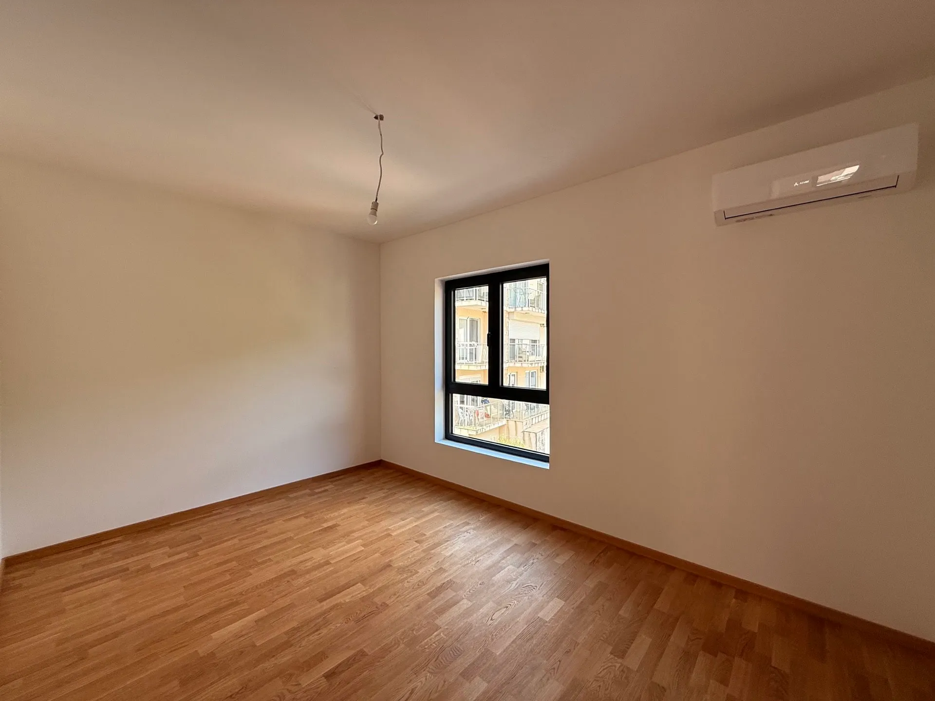 Empty room with laminate flooring, a window, and an AC unit. No furniture or specific bedroom features visible.