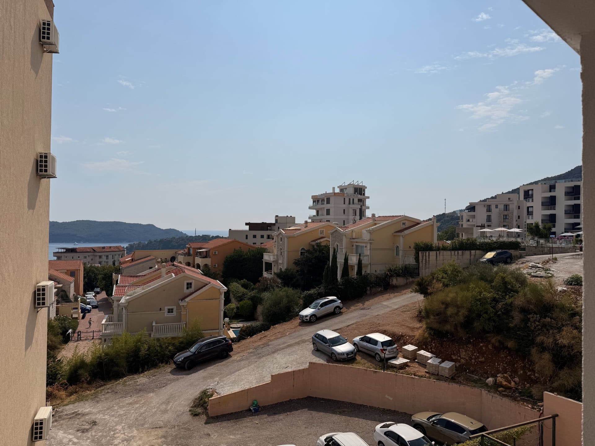 View from the apartment balcony in Bečići, Montenegro: a panorama of the residential complex, mountains, and the seaside on a sunny day.
