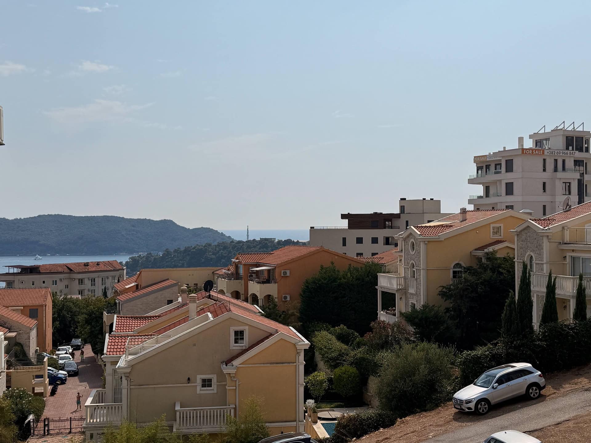 Panoramic view of the sea and residential complex in Bečići, Montenegro: cozy houses with tiled roofs and green hills.