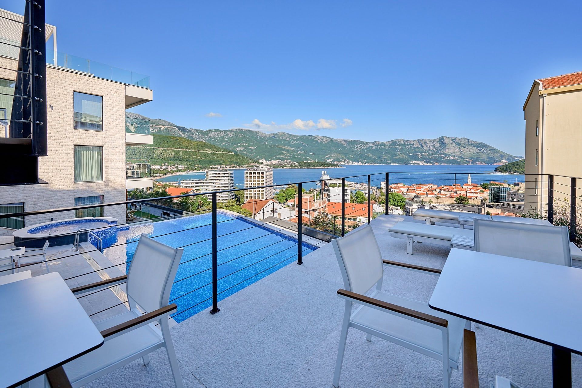 Terrace with a pool and sea and mountain views in Budva, Montenegro: modern furniture, sun loungers, and a panoramic landscape.