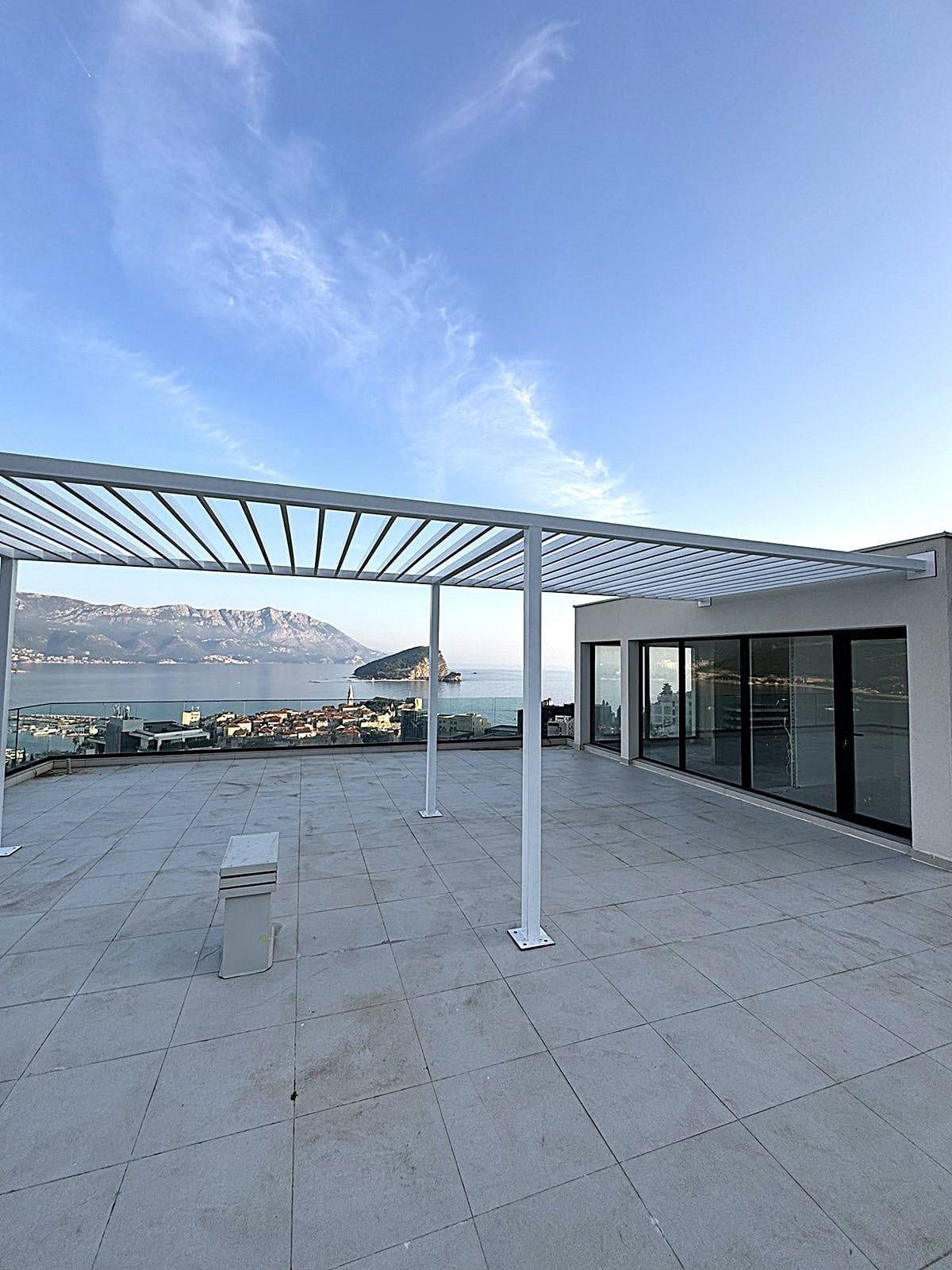 Spacious terrace with a pergola and panoramic views of the sea and island in Budva, Montenegro. Modern apartment.