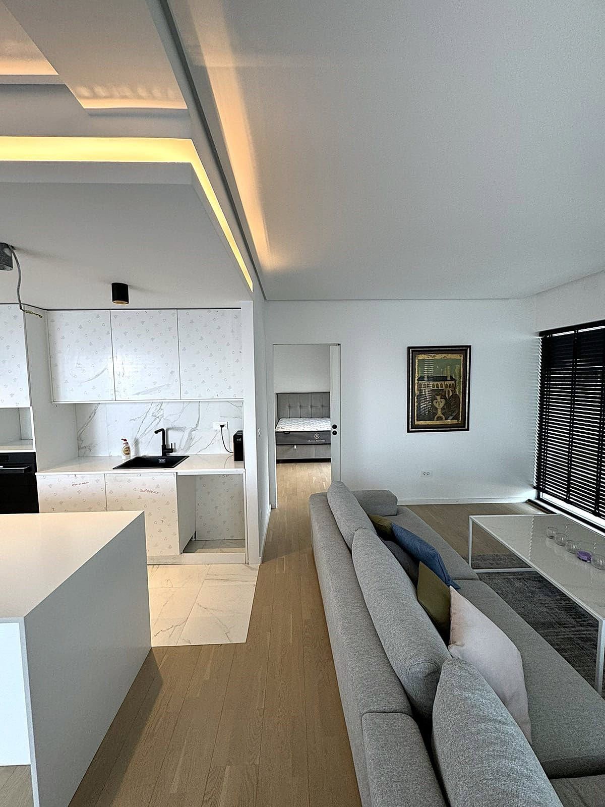 Modern living room with kitchen in an apartment, Budva, Montenegro: gray sofa, marble backsplash, and view of the bedroom.