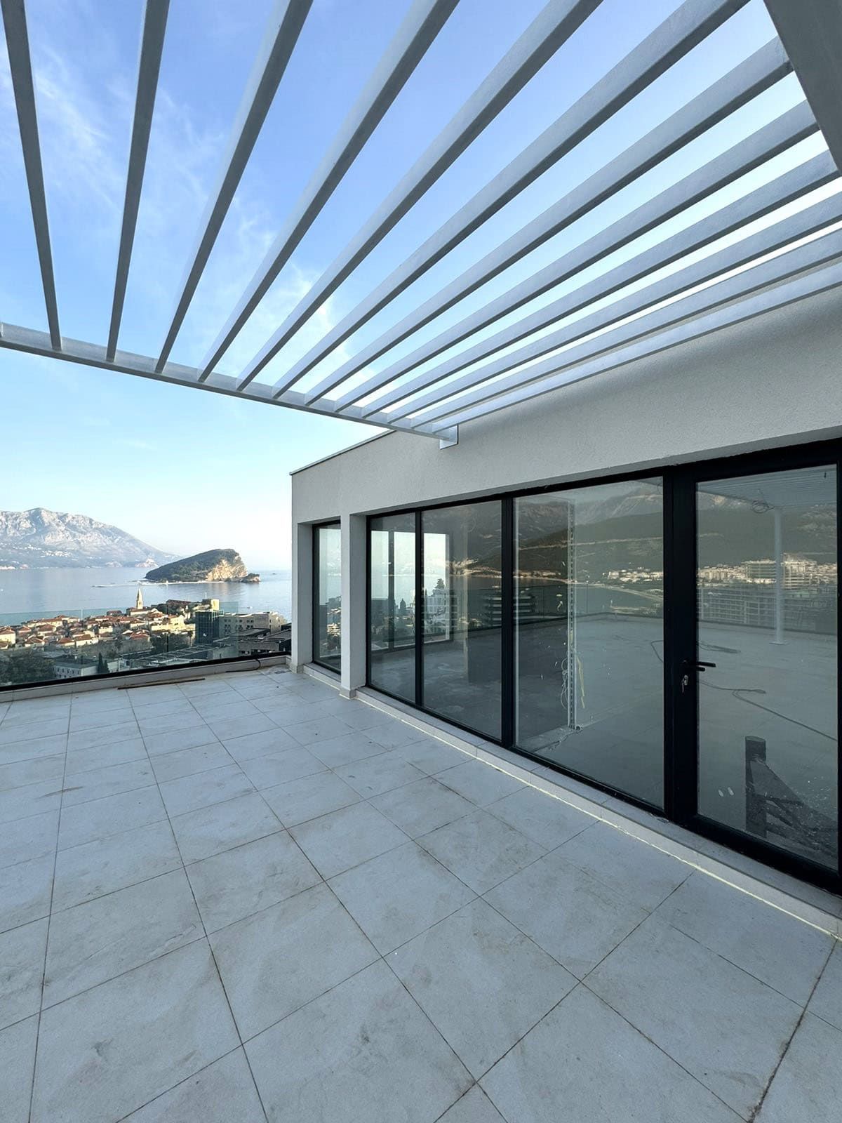 Spacious terrace with panoramic views of the sea and island in Budva, Montenegro, with an awning and panoramic glazing.