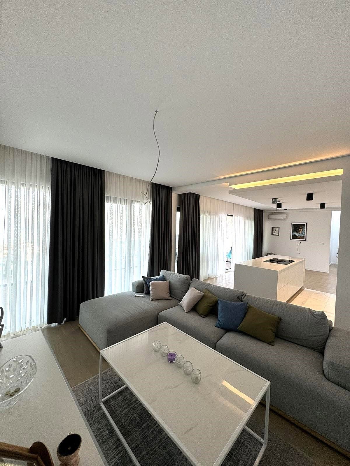 Modern living room with a gray sofa and kitchen island in an apartment in Budva, Montenegro. Stylish interior with panoramic windows...