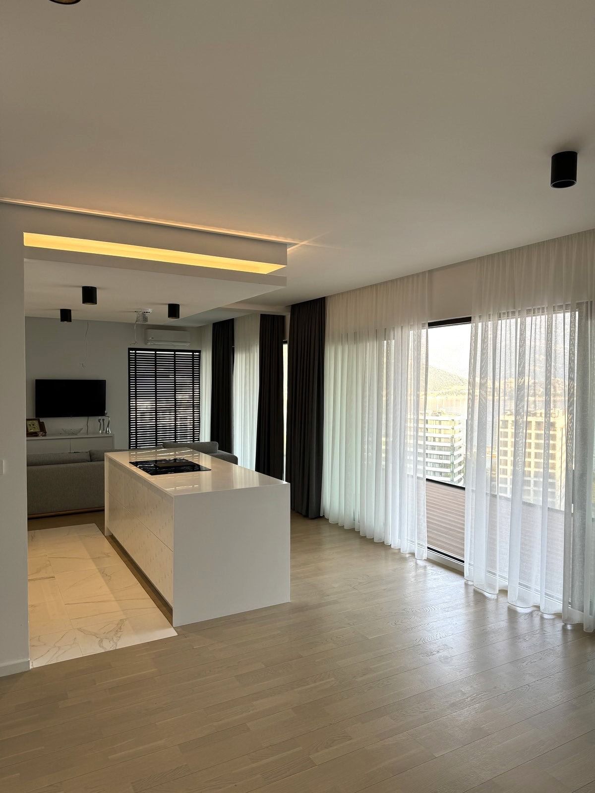 Modern kitchen-living room with an island in an apartment in Budva, Montenegro: panoramic windows, light finishes, and stylish design.
