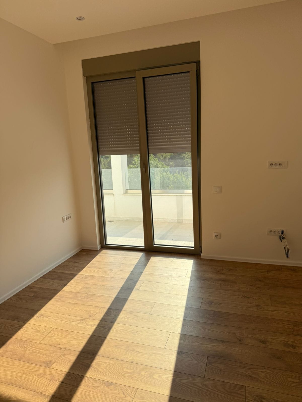 Bright bedroom in a new building in Tivat, Montenegro: wood-look laminate, panoramic door to the terrace, and roller shutters.