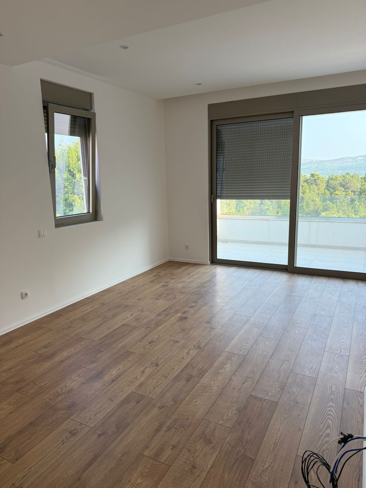 Bright living room in a new apartment in Tivat, Montenegro: wood-look laminate flooring, panoramic windows, and access to the terrace.