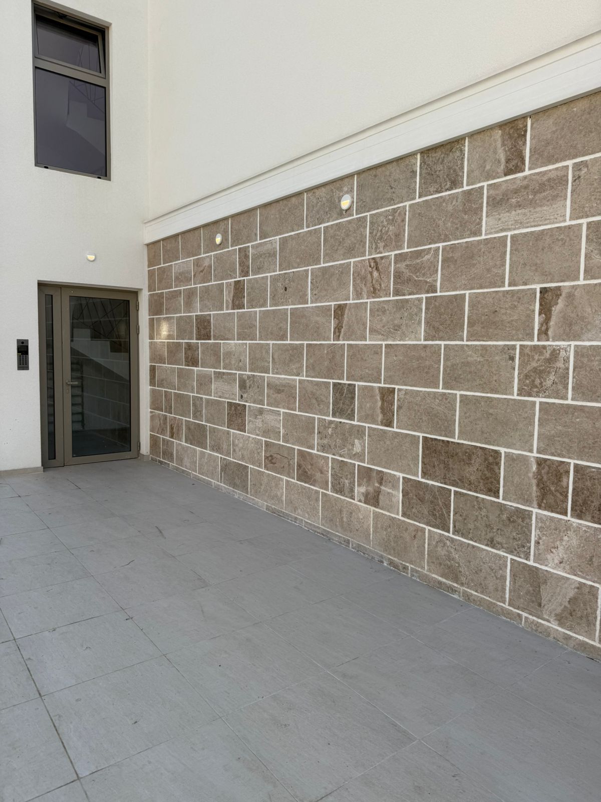 Facade of a modern residential building in Tivat, Montenegro: natural stone cladding, glass entrance area, and terrace.