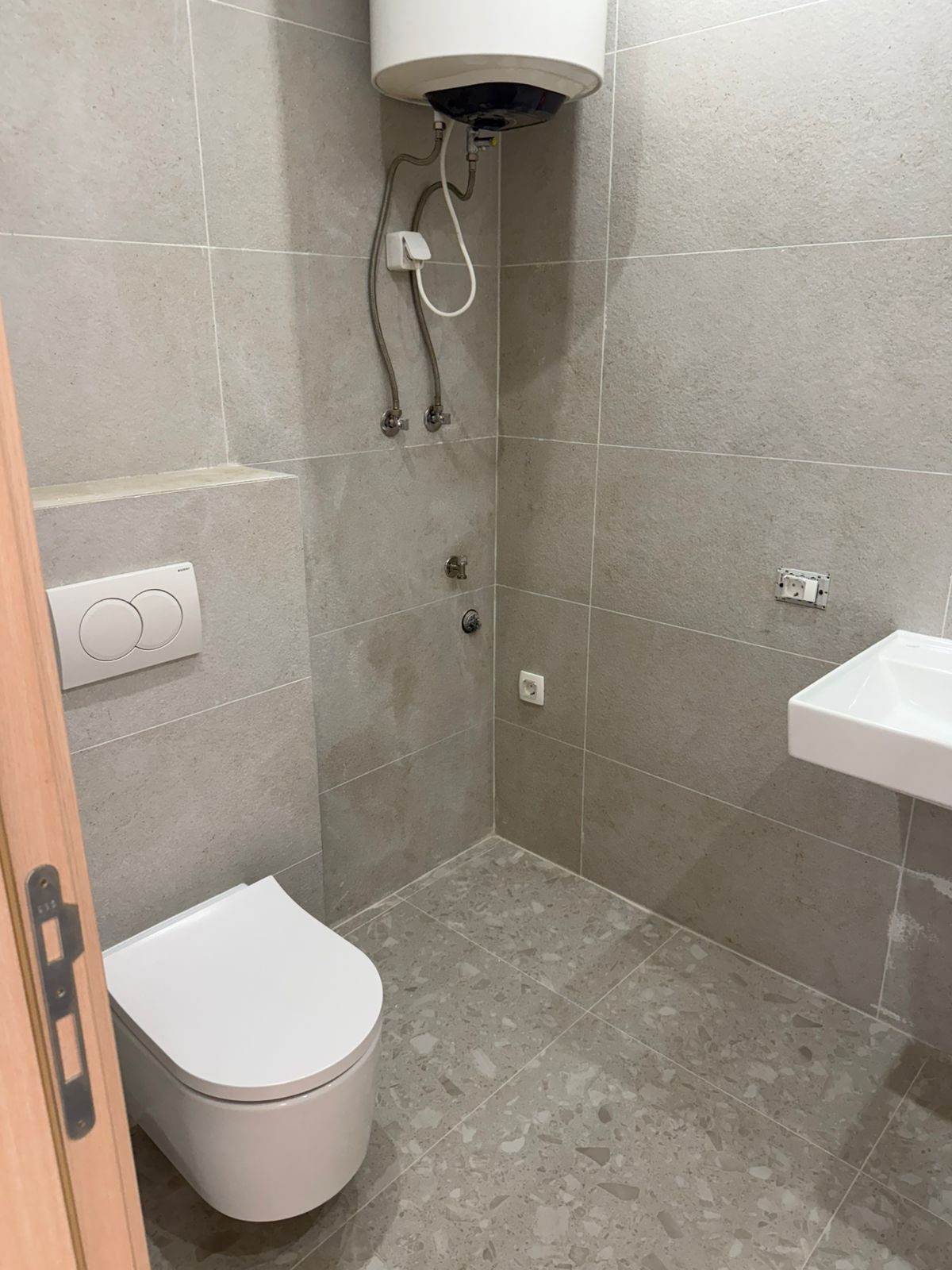 Modern bathroom in an apartment in Tivat, Montenegro: gray tiles, wall-mounted toilet, and boiler.