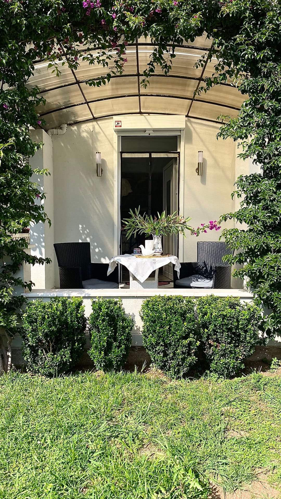 Cozy terrace with wicker furniture and a garden in an apartment in Petrovac, Montenegro. View of a green courtyard and awning.