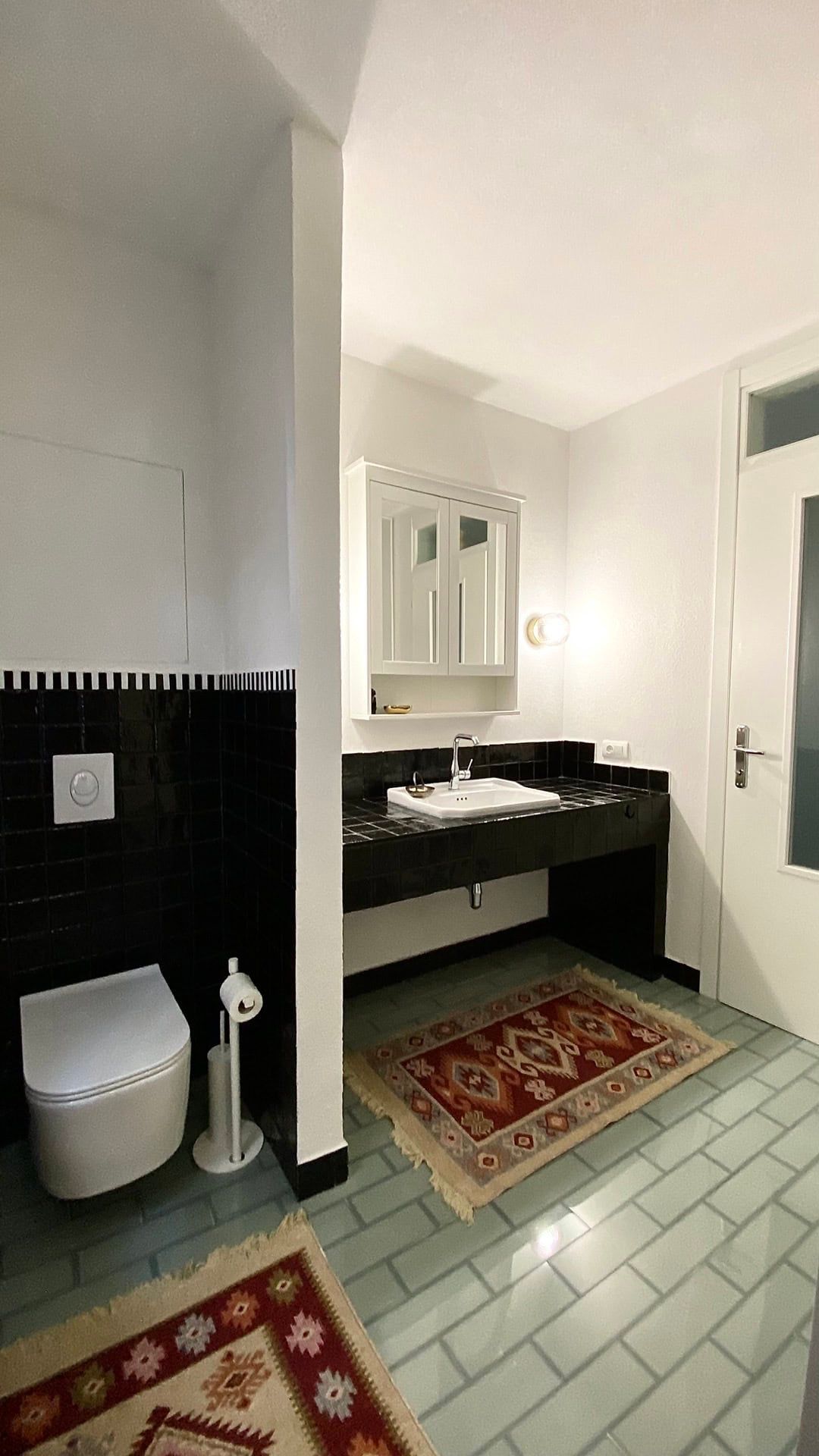 Modern bathroom in an apartment in Petrovac, Montenegro: black tile, wall-mounted toilet, and vintage rugs.