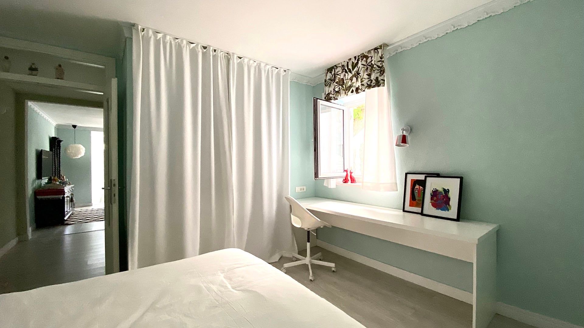 Bedroom in an apartment in Petrovac, Montenegro: light walls, a workspace by the window, white furniture, and a view of the adjacent room.