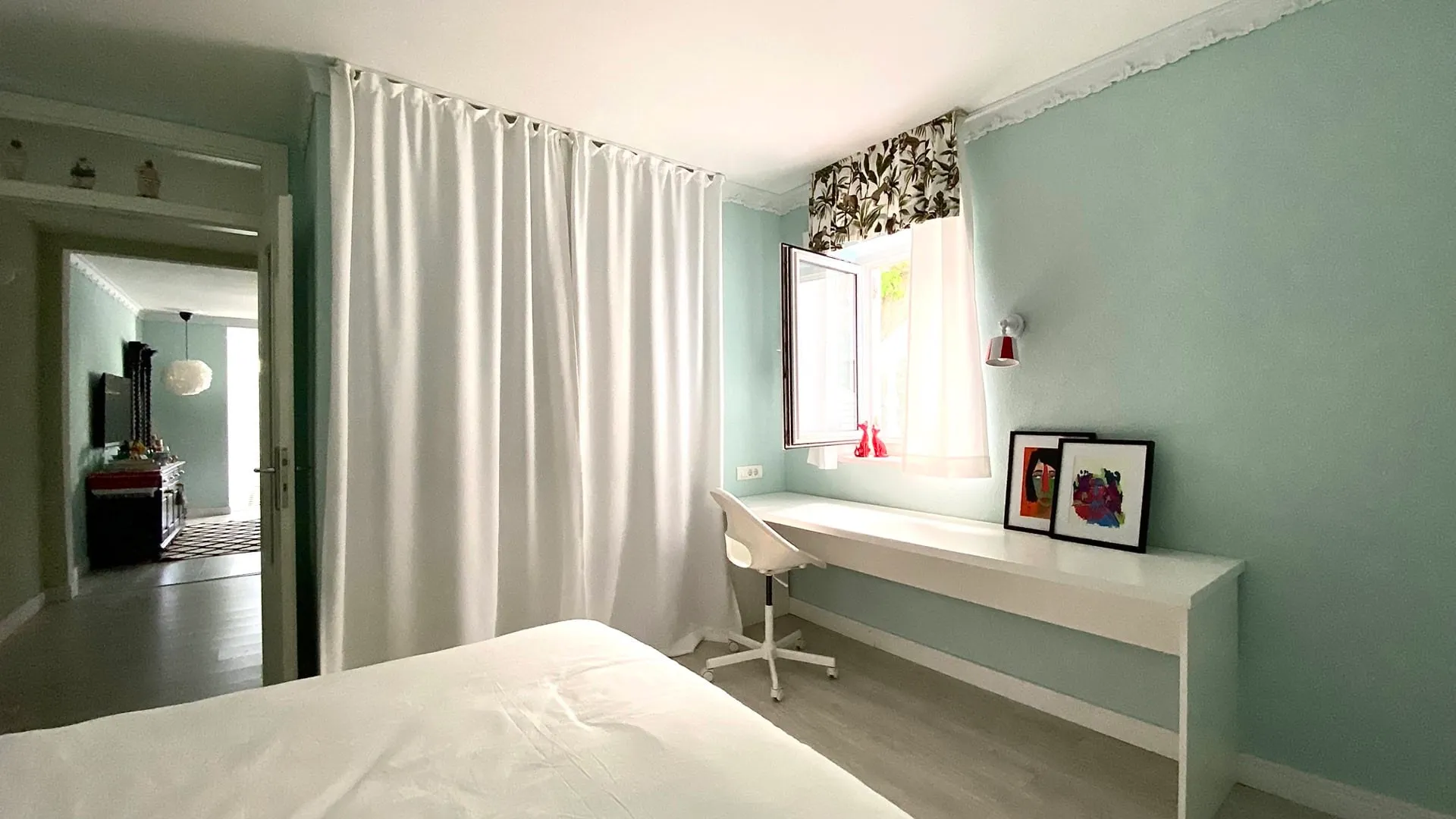 Bright bedroom with a white bed, desk by the window, and light blue walls.