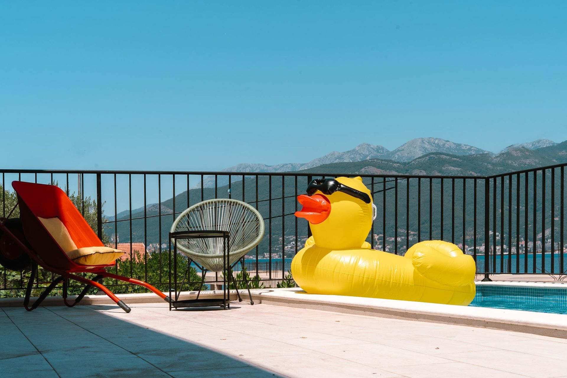 Swimming pool on the villa terrace in Krašići, Montenegro: view of the sea and mountains, designer lounge chairs, and an inflatable duck.