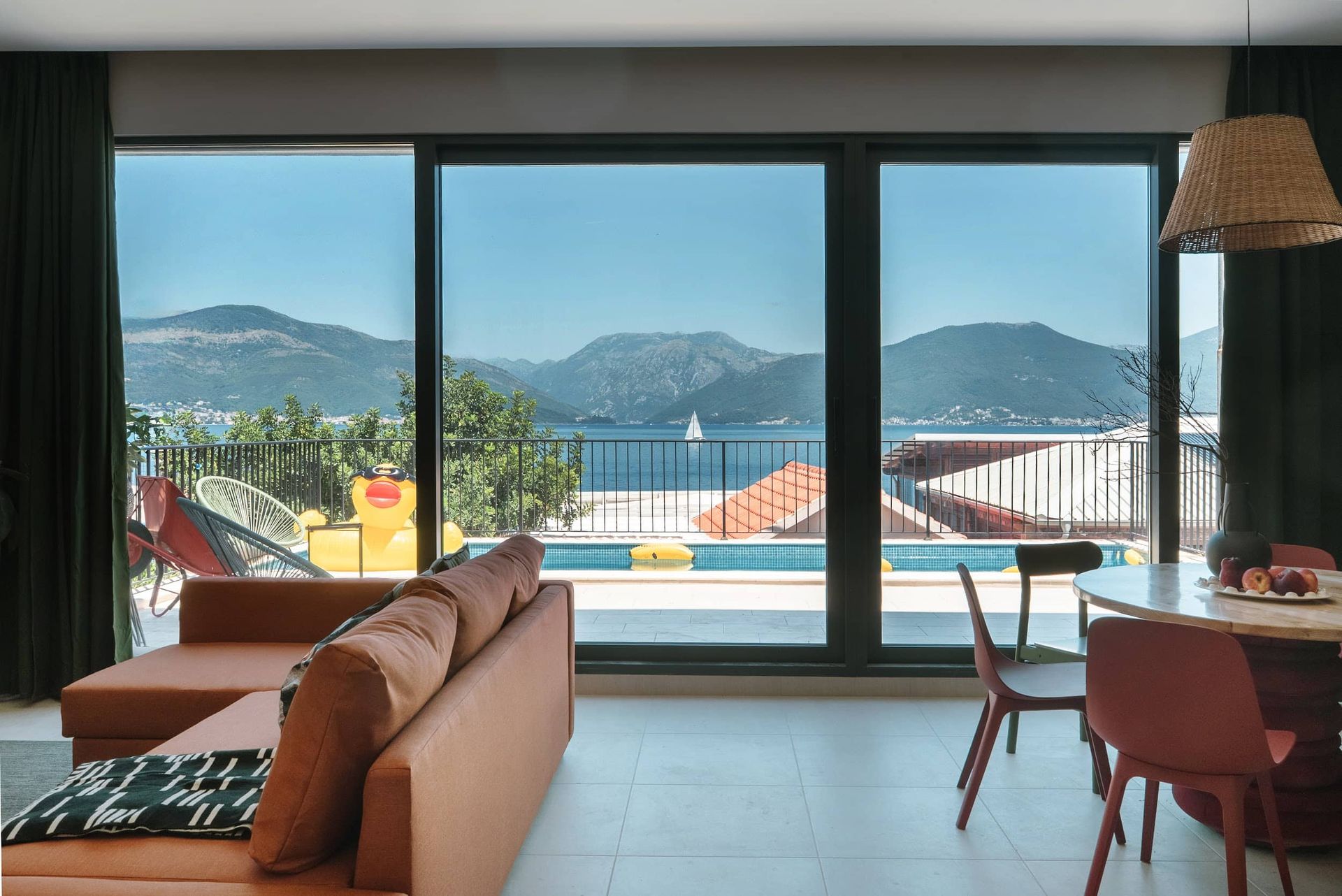 Living room of a villa in Krašići, Montenegro: panoramic view of the sea, mountains, and swimming pool through large windows, modern interior.