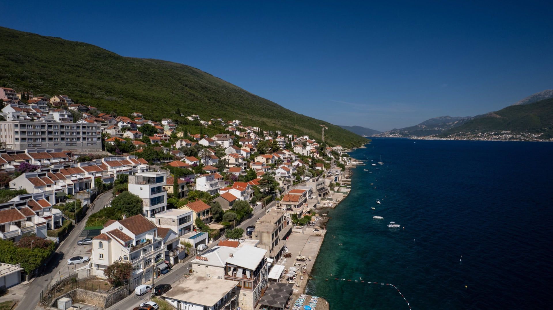 Panoramic view of villas in Krašići, Montenegro: coastal development by the sea with mountains in the background, aerial view.