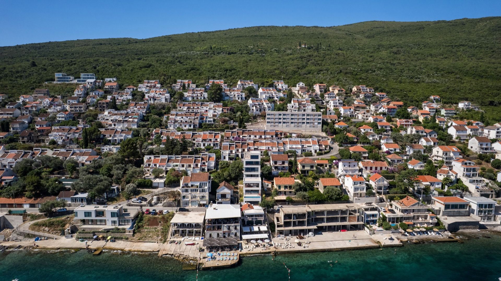 Aerial view of villas and a residential complex in Krašići, Montenegro: coastal development by the sea with terraces and a beach.