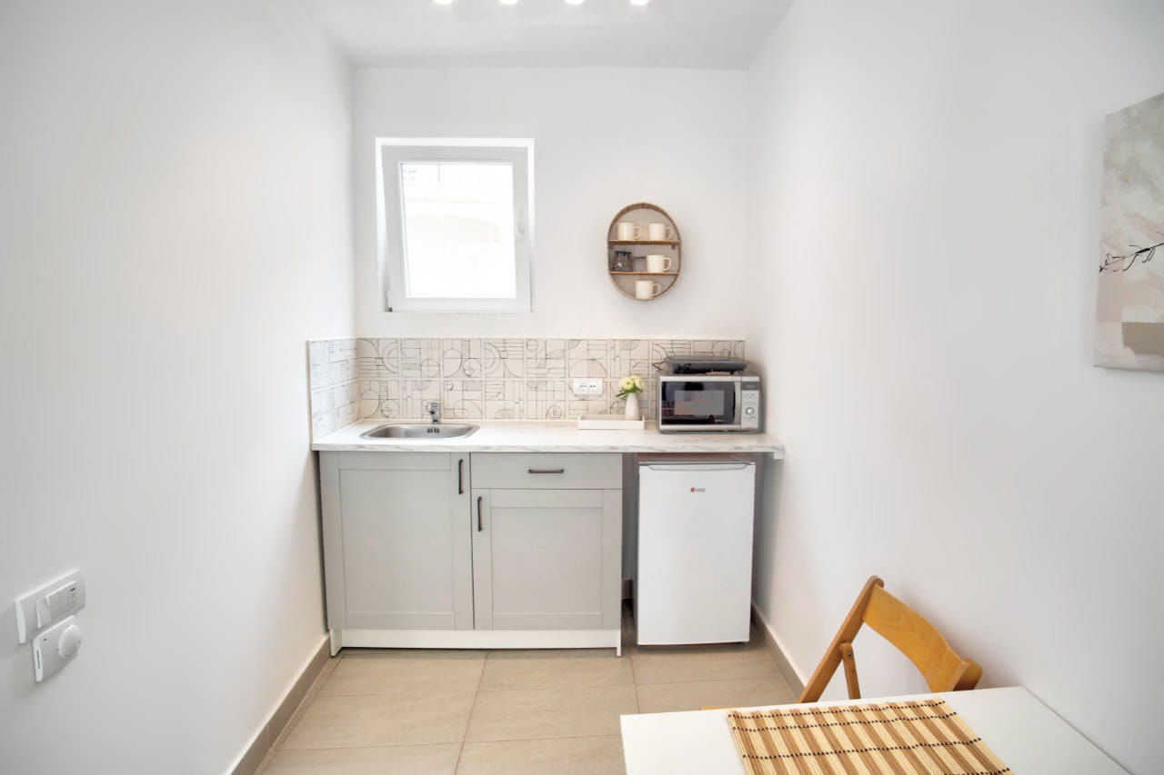 Compact bright kitchen in an apartment in Baošići, Montenegro: gray cabinets, patterned tile, and a dining area.