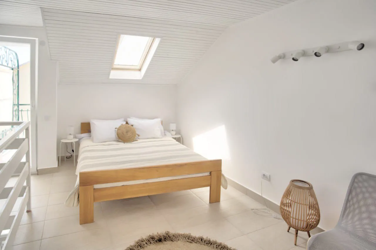 Bright bedroom with a wooden bed, skylight in sloped ceiling, and white walls.