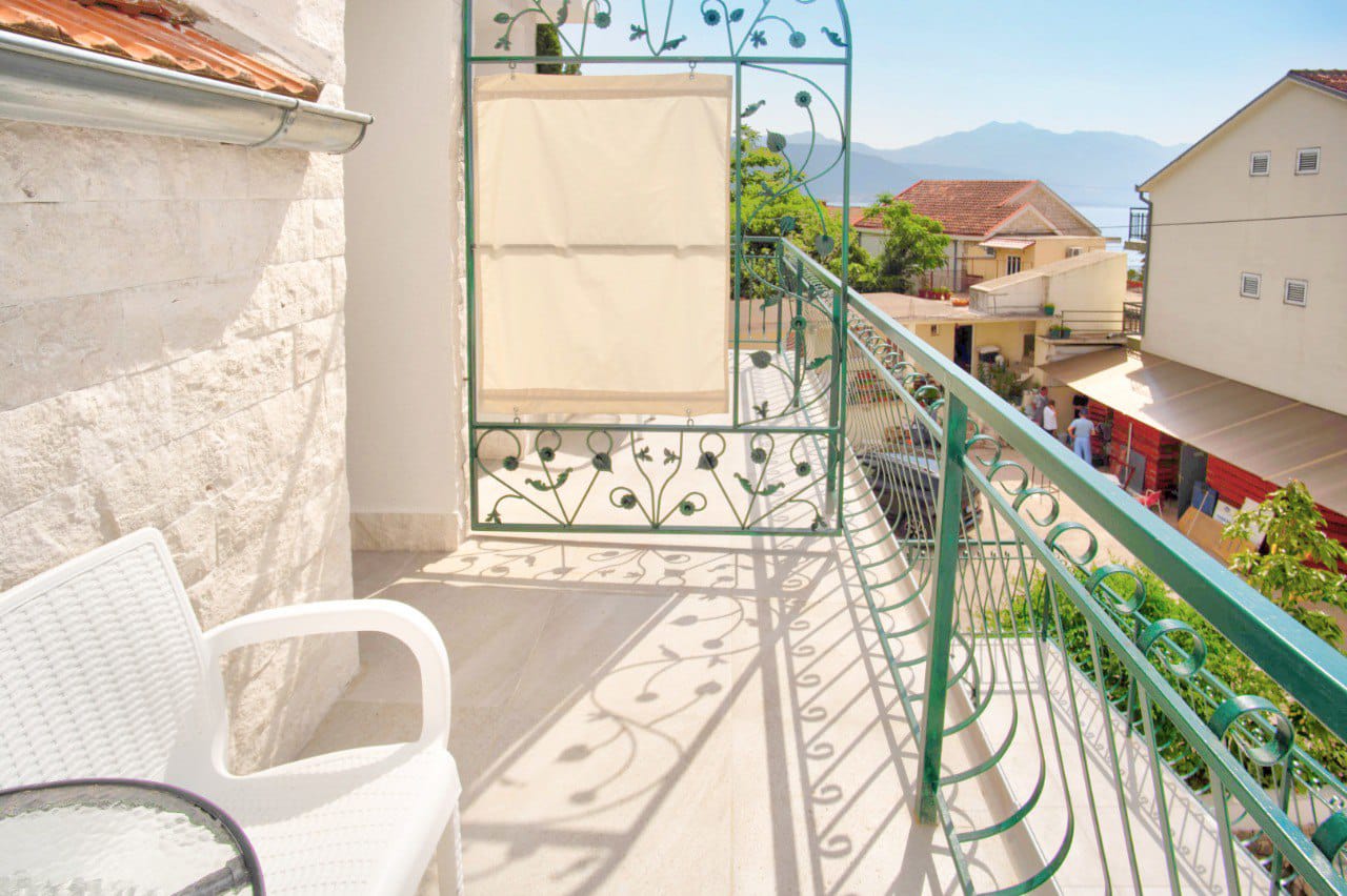 Balcony with white plastic chair and green wrought iron railing overlooking a street and mountains.