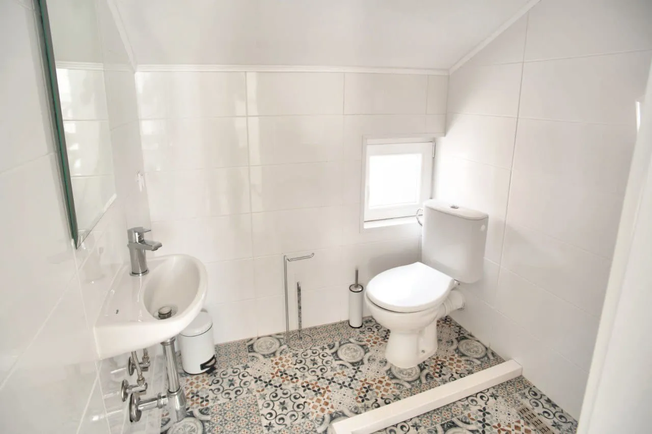 Small white bathroom featuring a toilet, wall-mounted sink, and patterned tile flooring.