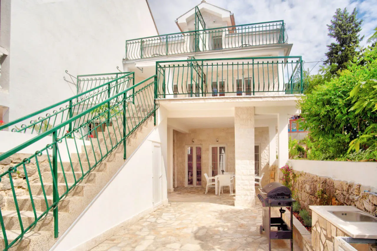 House exterior with stone stairs, green railings, covered patio with white furniture and a grill.