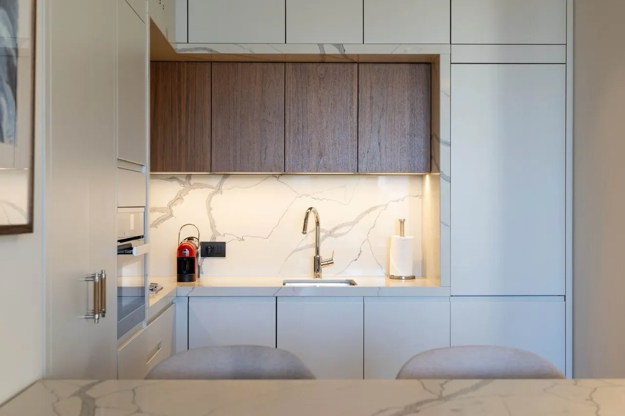 Modern kitchen featuring white cabinets, wood upper units, marble countertop, sink with chrome faucet, and a red coffee machine.