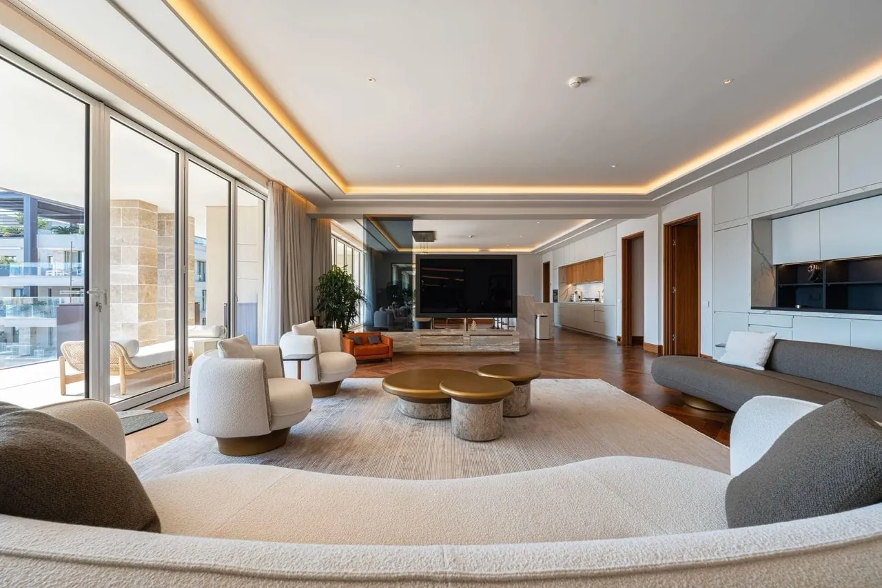 Modern living room with sofas, coffee table, and TV on a fireplace, featuring large floor-to-ceiling windows.