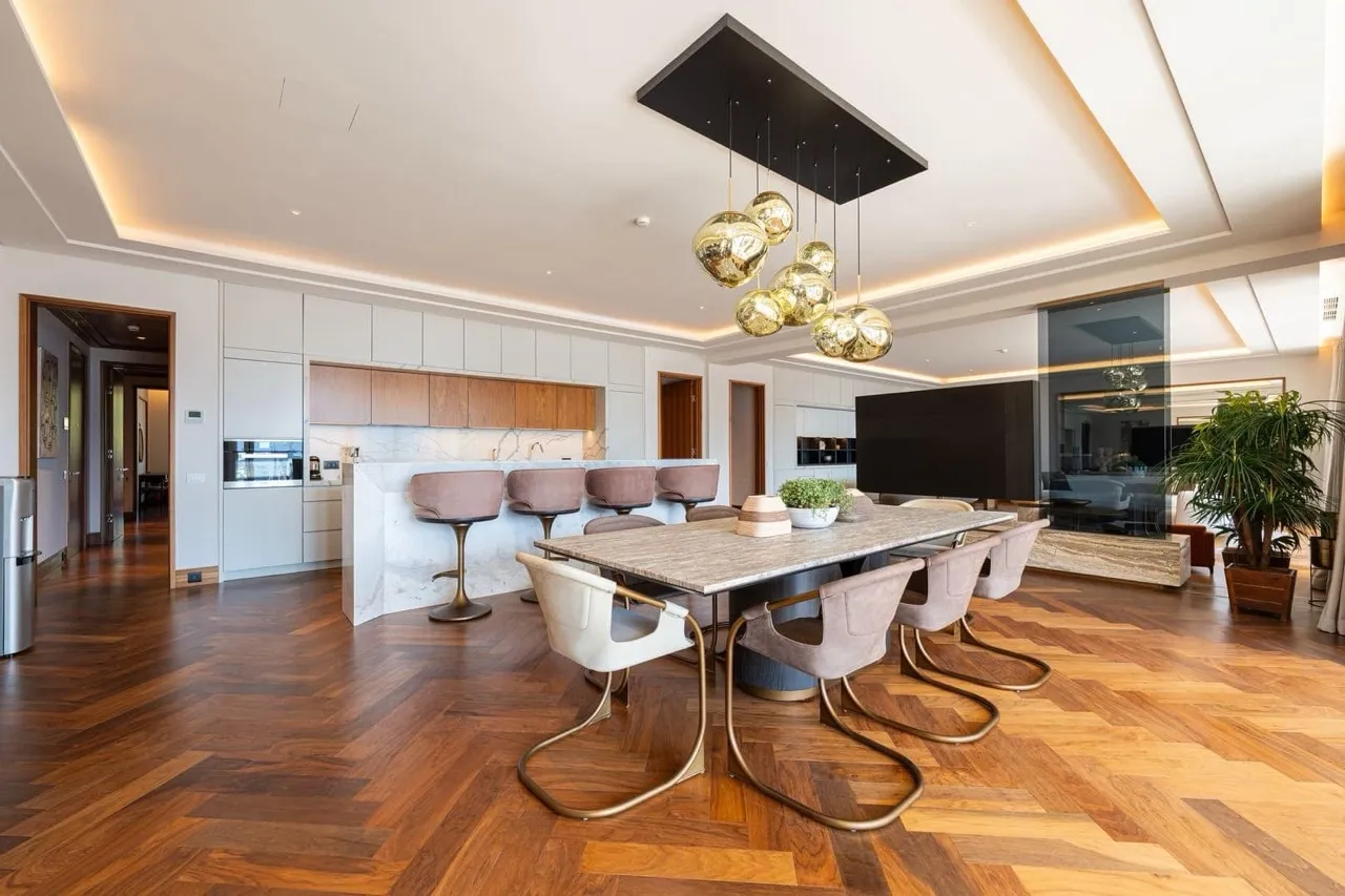 Open plan space featuring a dining table, kitchen island with stools, and herringbone wood floors.