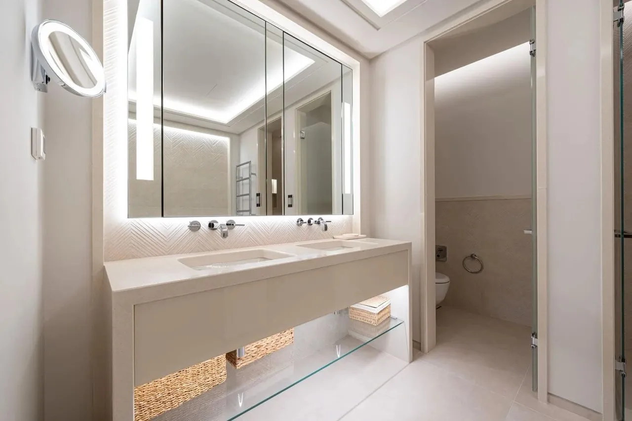 Modern bathroom featuring a double vanity, large backlit mirror, and separate toilet area.