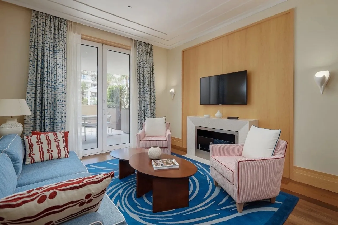Living room with blue sofa, pink armchairs, coffee table, and TV above a fireplace set into a wood panel wall.