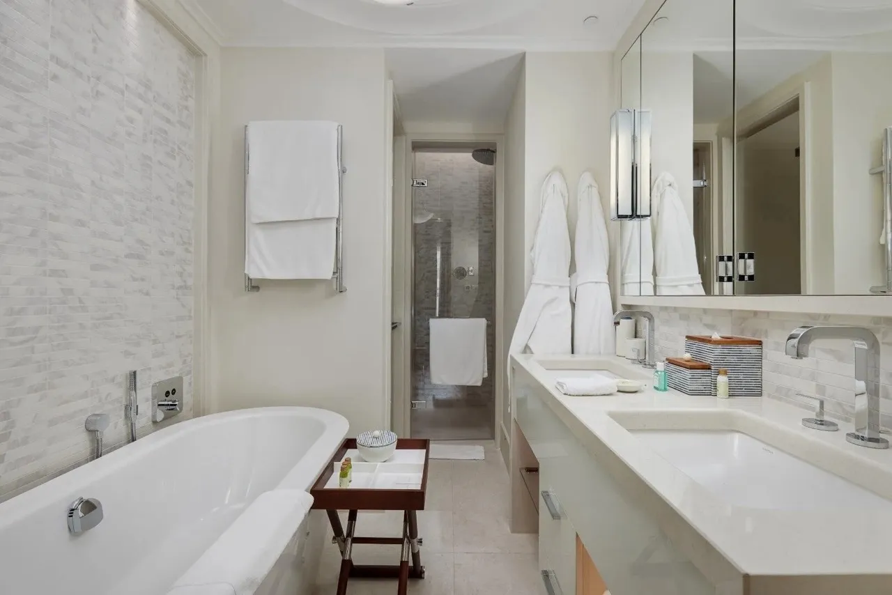 Modern bathroom featuring a white bathtub, double vanity sink, glass shower enclosure, and hanging robes.