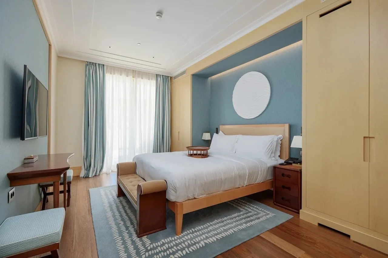 Bedroom featuring a double bed, blue accent wall, wooden wardrobe, desk, and bench.