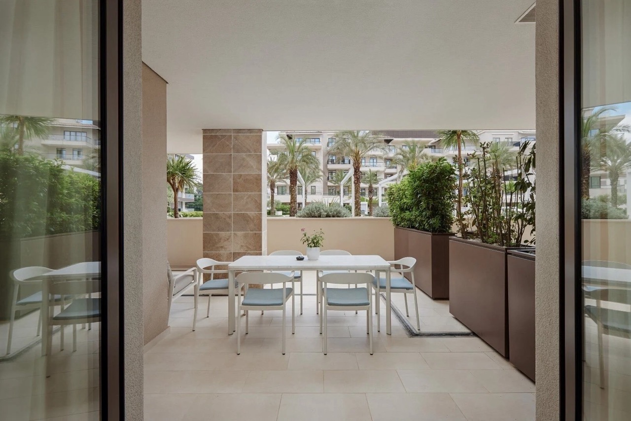Spacious terrace with dining area in an apartment in Porto Montenegro, Tivat, Montenegro, overlooking palm trees and the complex.