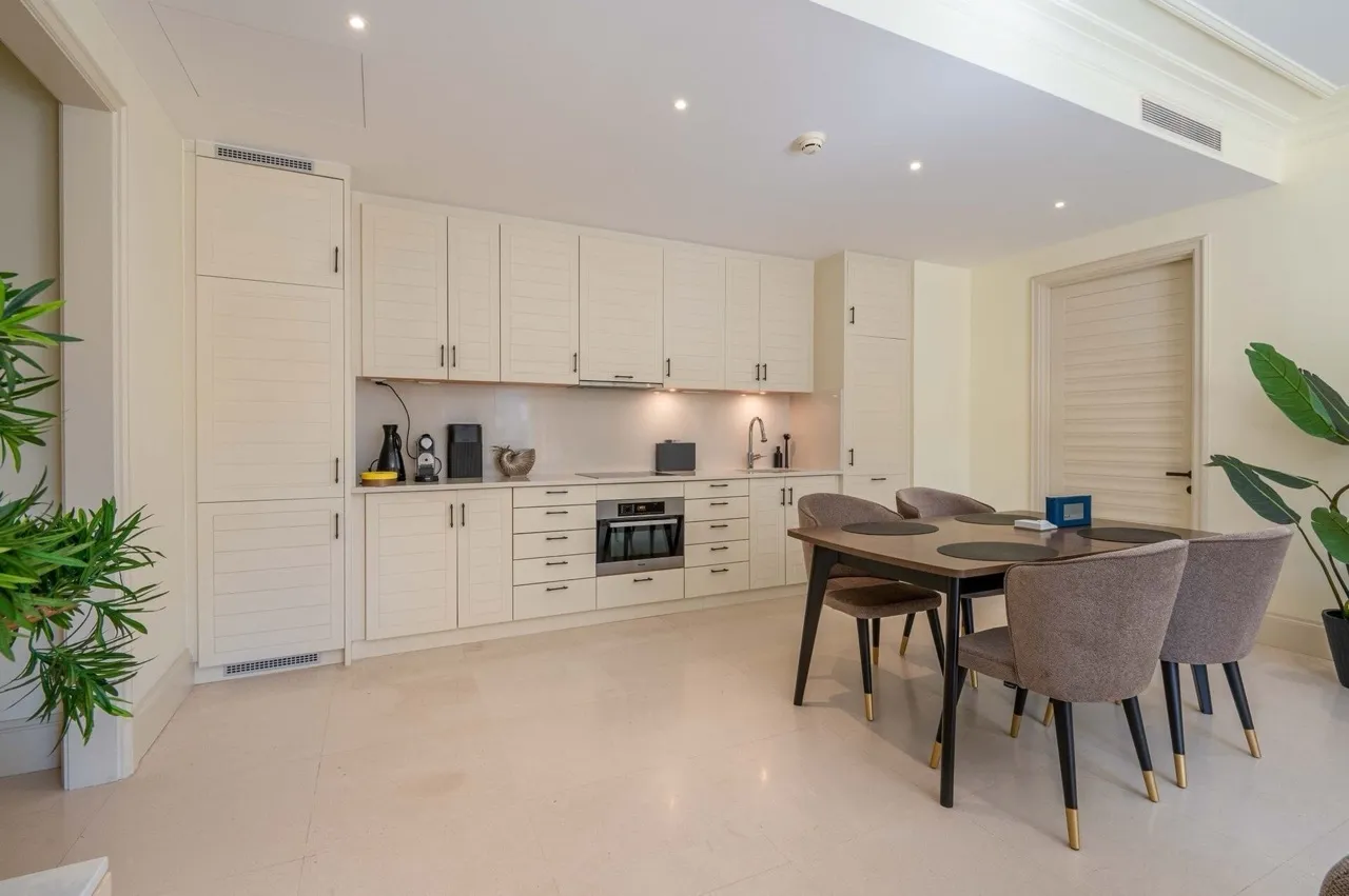 Modern kitchen with white cabinetry, built-in appliances, and a dining table with grey upholstered chairs.