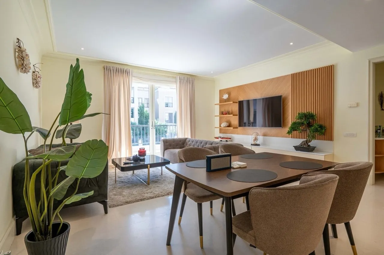 Living room featuring a sofa, coffee table, dining set with chairs, and TV mounted on a wood panel wall.