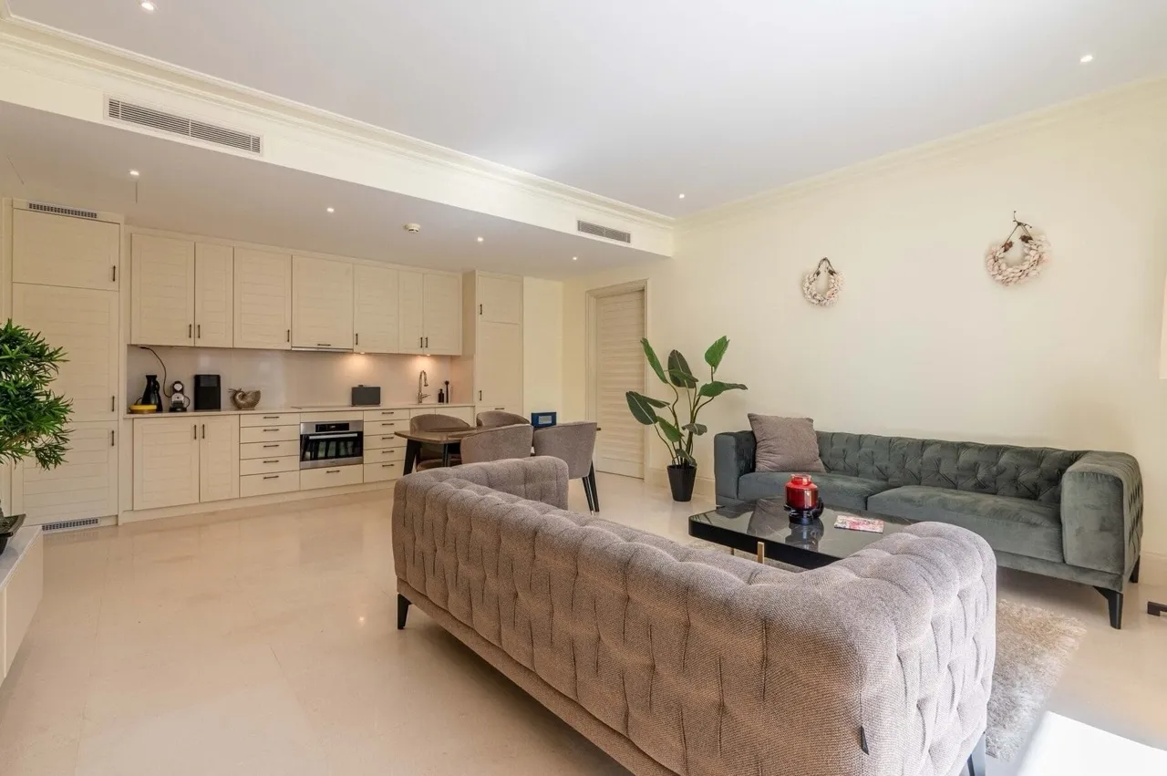 Bright living room with grey sofas and an open kitchen visible in the background.