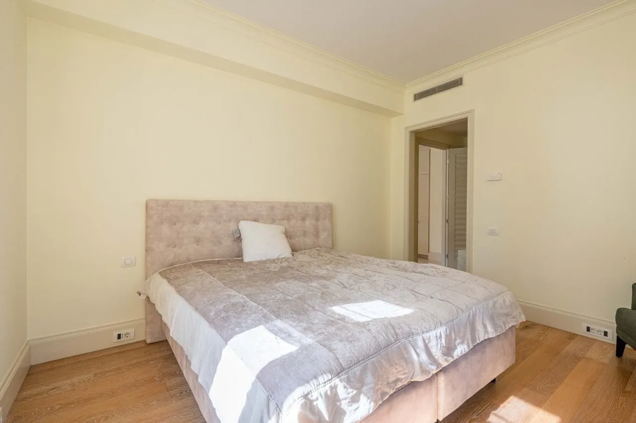 Bedroom featuring a beige double bed with tufted headboard, wooden flooring and cream walls.
