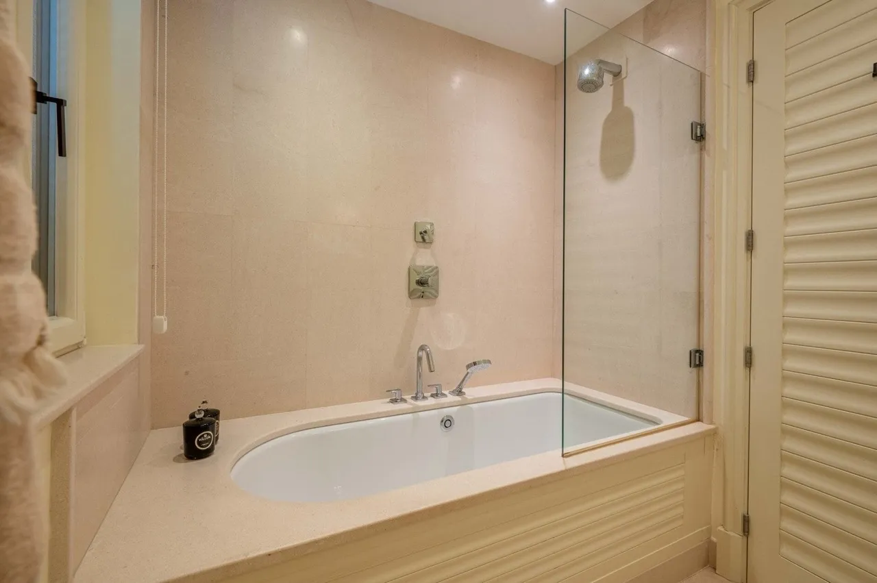 Bathroom featuring a white bathtub, shower fixture, and glass partition against beige tiled walls.