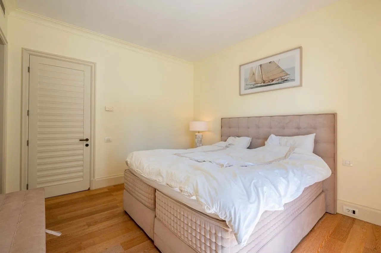Bedroom featuring a double bed with beige headboard, bedside lamp, wooden floor, and nautical artwork.