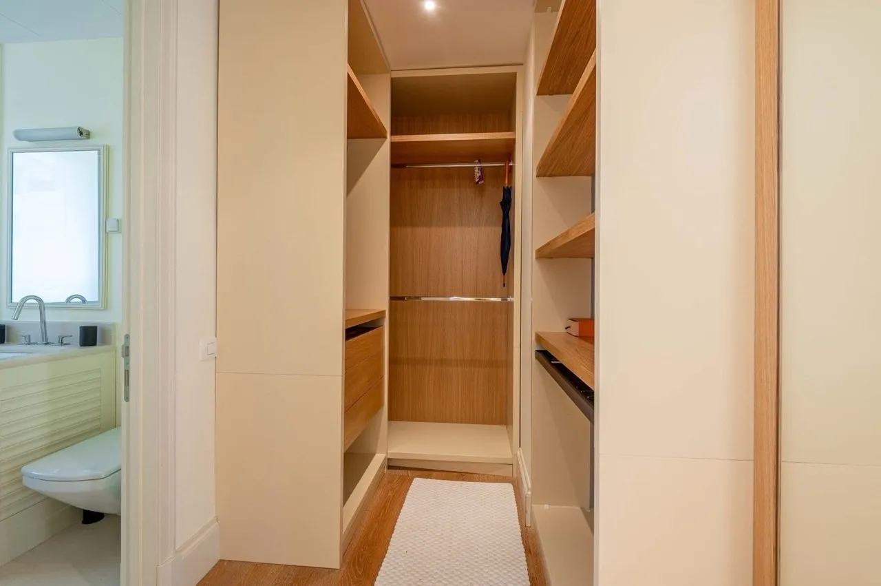 Built-in wooden walk-in closet with shelves and hanging rod, adjacent bathroom visible through door.