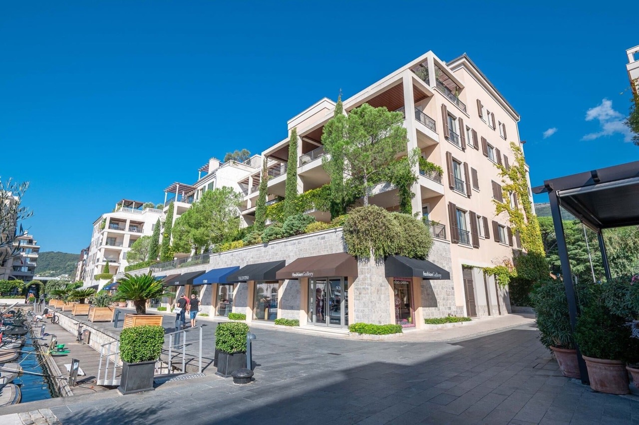 Facade of a luxury residential complex in Porto Montenegro, Tivat, Montenegro, with shops and a waterfront promenade by the yacht marina.